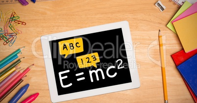 Directly above shot of formula in digital tablet with color pencils and school supplies on wooden ta