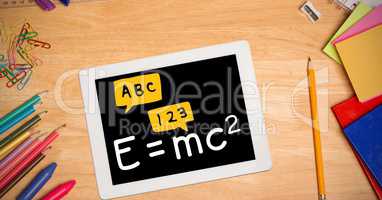 Directly above shot of formula in digital tablet with color pencils and school supplies on wooden ta