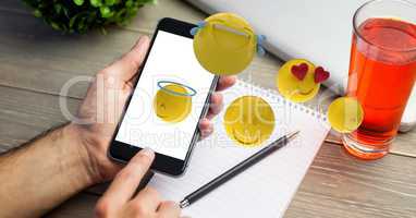 Hands using mobile phone while emojis flying over table