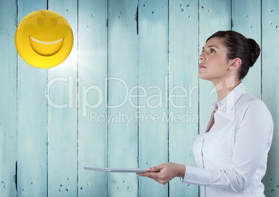 Business woman with tablet looking up at emoji and flare against blue wood panel