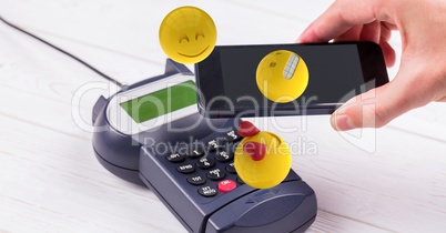 Digitally generated image of hand holding smart phone over credit card reader with emojis