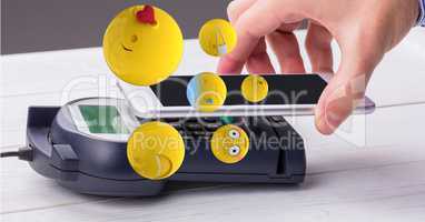 Digital composite image of hand making NFC payment with emojis flying over