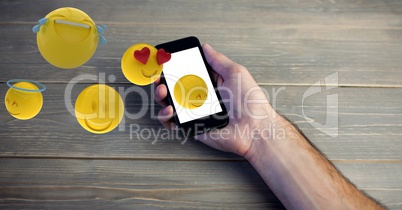Digital composite image of hand holding smart phone while emojis coming out of it