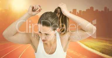 Female runner tying up hair on track against orange flares against skyline