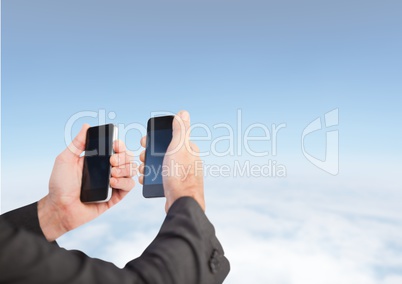 Hands holding two phones at same time against blue sky
