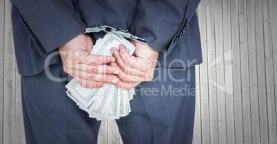 Close up of business man's hands behind back with money and handcuffs against grey wood panel