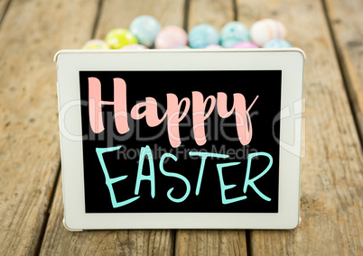 Pink and blue type on tablet on wood table with easter eggs