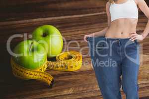 Midsection of woman in loose jeans by salad bowl on table