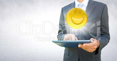 Business man mid section with tablet and emoji with flare against white wall
