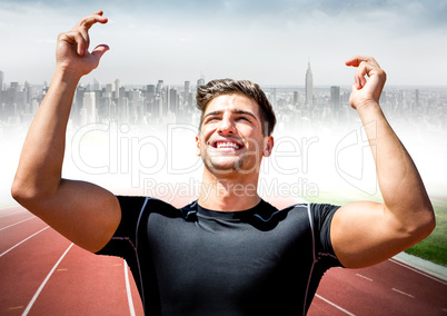 Male runner with hands in air on track against blurry skyline