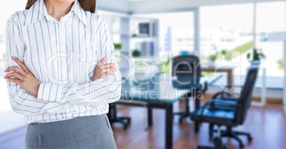 Midsection of businesswoman with arms crossed standing against desk in office