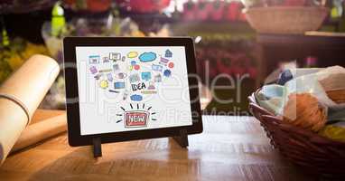 Various icons and text in digital tablet by basket and paper on table