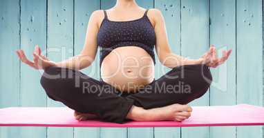 Pregnant woman meditating against blue wood panel