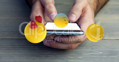 Cropped image of hands holding mobile phone with various emojis at wooden table