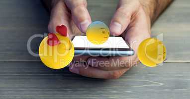 Cropped image of hands holding mobile phone with various emojis at wooden table
