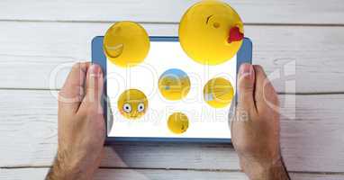 Digitally generated image of emojis flying over hands holding digital tablet