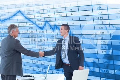 Happy businessmen shaking hands against stock data background