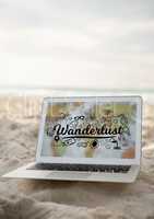 Laptop on sand showing black wanderlust doodles against blurry map