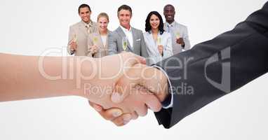 Cropped image of business people doing handshake with employees holding champagne in background