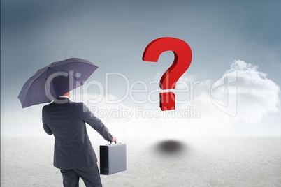Businessman with umbrella and briefcase looking at red question mark