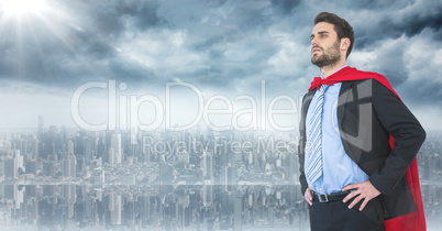Business man superhero with hands on hips against skyline and flare