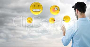 Back of man with emojis and flare against sky with clouds