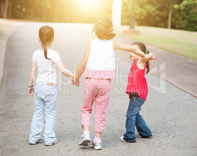 Asian children holding hands walking outdoor.