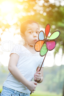 Asian child blowing windmill outdoors.