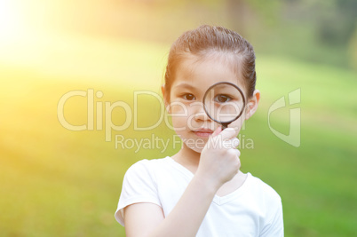 Asian little girl with magnifier glass at outdoors.