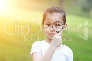 Asian little girl with magnifier glass at outdoors.