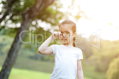 Asian little girl exploring nature with magnifier glass at outdo