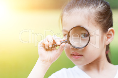 Asian child with magnifier glass at outdoors.