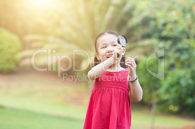 Little girl exploring nature with magnifier glass at outdoors.