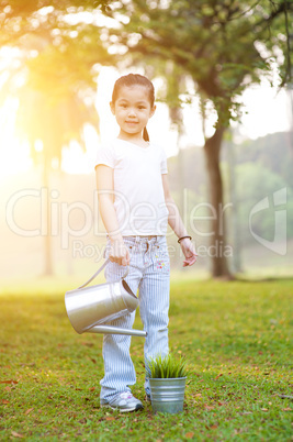 Asian kid watering plant outdoors.