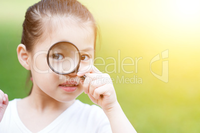 Asian kid with magnifier glass at outdoors.