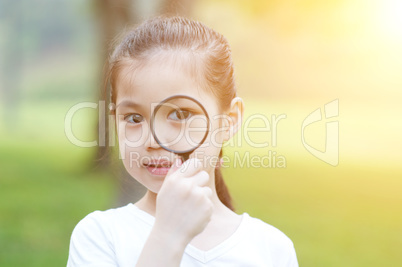Little girl with magnifier glass at outdoors.
