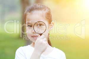 Little girl with magnifier glass at outdoors.