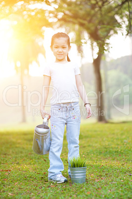 Asian little girl watering plant outdoors.