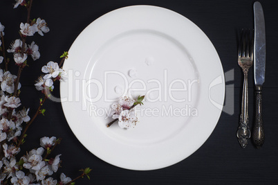 Empty white plate with cutlery on a black wooden surface
