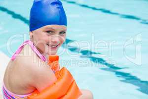 Smiling girl with swim cap sitting near poolside