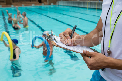 Swim coach writing on clipboard near poolside