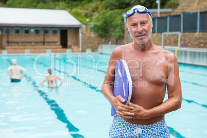 Smiling senior man holding kickboard at poolside