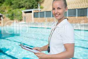 Smiling swim coach holding clipboard at poolside