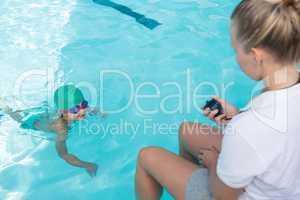 Female trainer monitoring time of boy swimming in pool