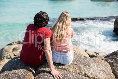 Couple sitting on rock against sea