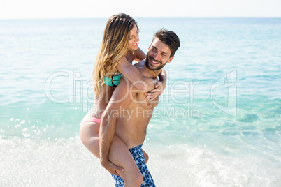 Boyfriend piggybacking girlfriend on shore at beach