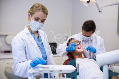 Dentist holding dental tool while his colleague examining patient in background