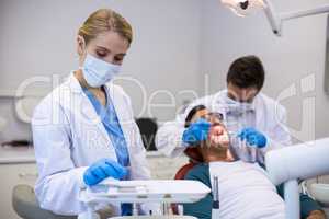 Dentist holding dental tool while his colleague examining patient in background