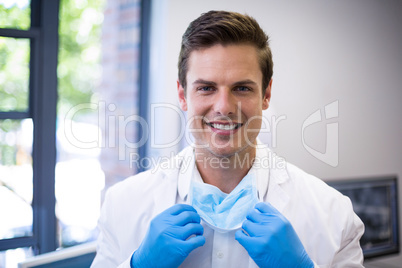 Portrait of happy dentist holding surgical mask