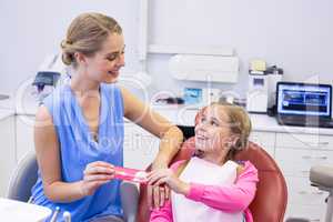 Mother giving tooth brush to daughter at dental clinic